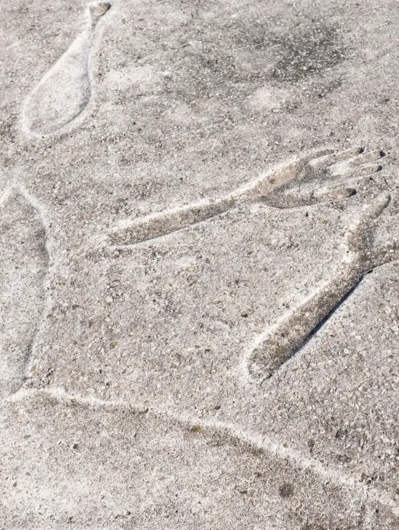 Round concrete sculptural with an impression of a person&#039;s body in a seated position, legs outward in a v-shape, hands and forearms in the middle fingers stretching outward.