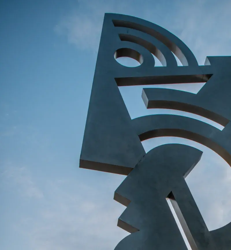 Large silver colored sculpture in the shape of an abstract head on a long neck. The photo is taken from ground level, looking up.