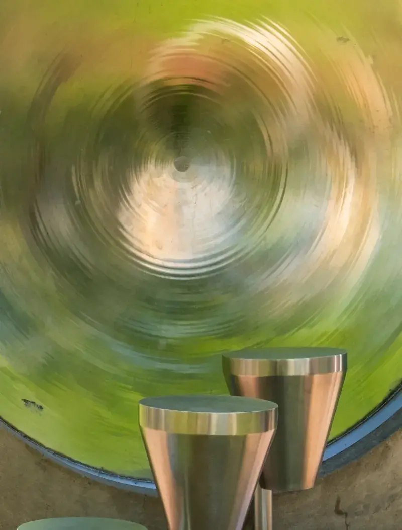 Close up of multiple silver metal drums of various types and sizes. The middle drum reflects the green grass surrounding it.