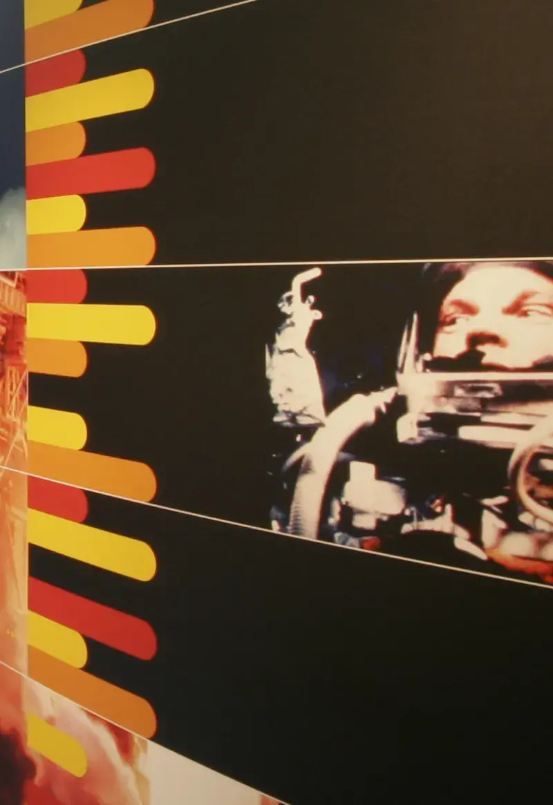Close up of an image of an astronaut and a space shuttle on a black background and a timeline on a white background are printed on 2 curved panels held up on metal legs.