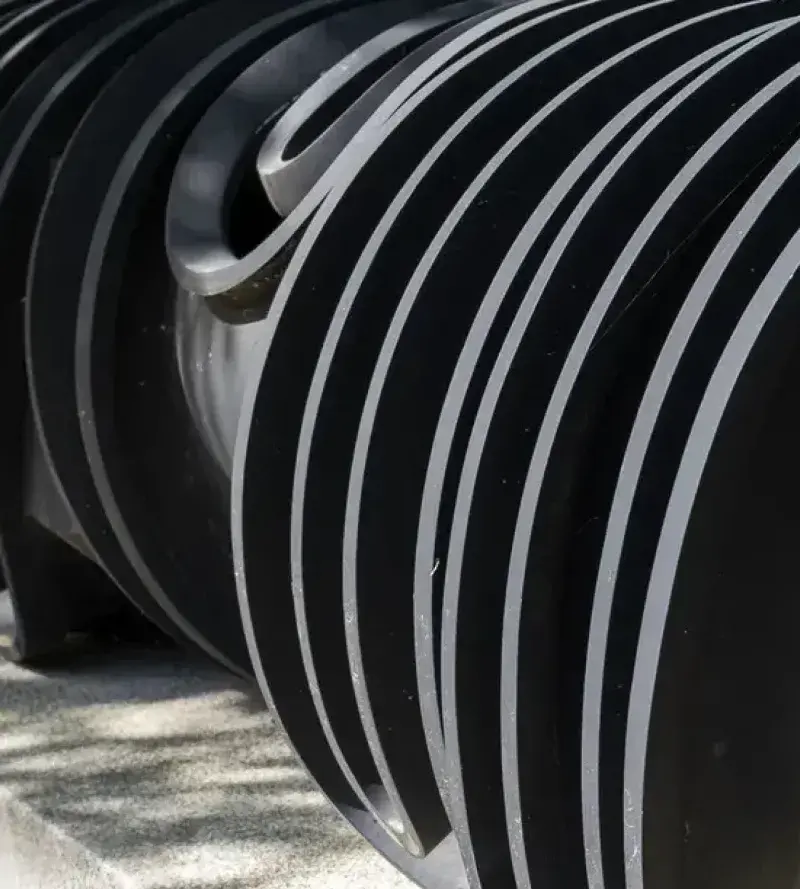 Close up of a dark metal sculpture of curvilinear forms sits on a gray stone base.