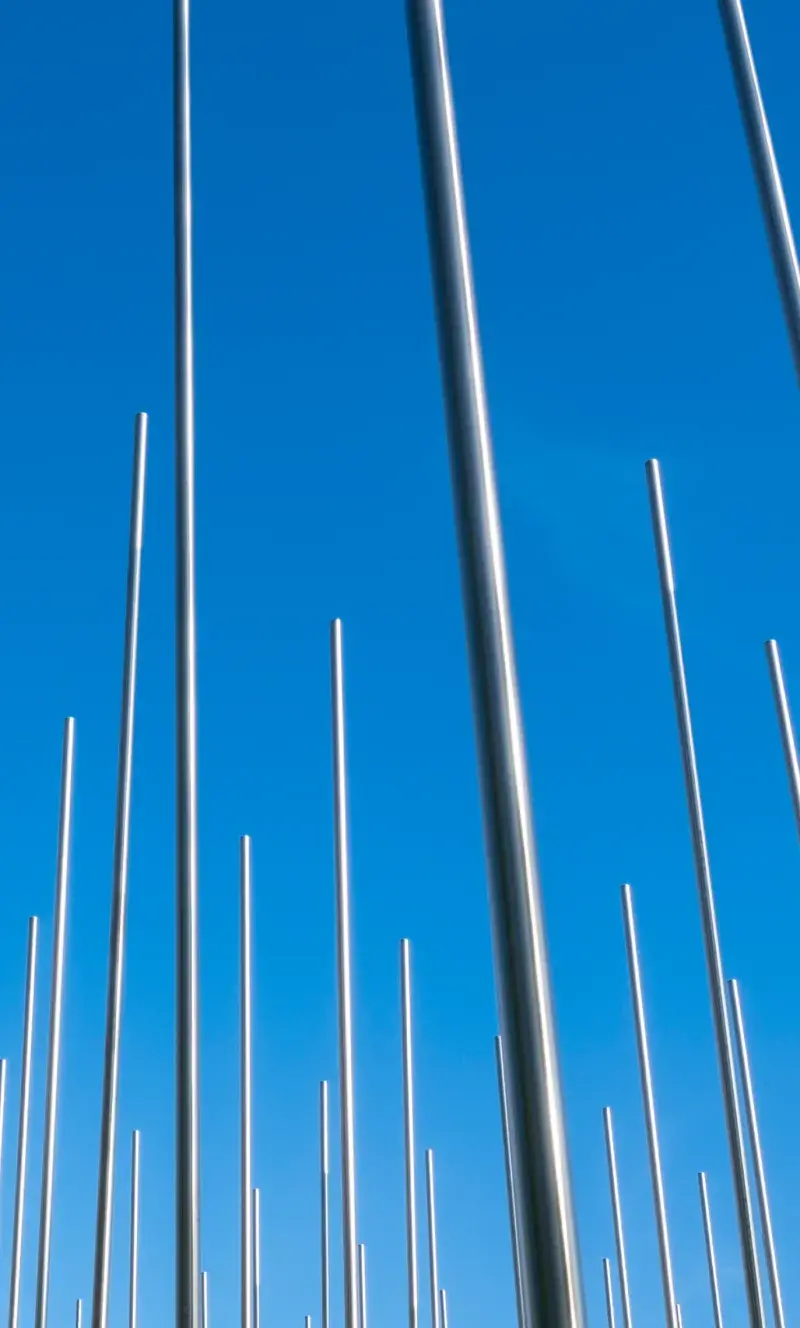 Tall, thin, silver metal rods stand in a grid in front of a bright blue sky.